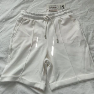 Vita shorts med snörning XS - Snygga vita shorts med elastisk midja och snörning framtill. De har raka ben, fickor på sidorna och uppvikta benslut för en clean och sportig look. Perfekta för varma dagar och chill outfits.
