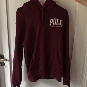Vinröd hoodie från Polo Ralph Lauren - Snygg vinröd hoodie från Polo Ralph Lauren med broderad logga på bröstet. Klassisk känguruficka, huva med snörning och långa ärmar. Nypris 2200kr mitt pris 900 