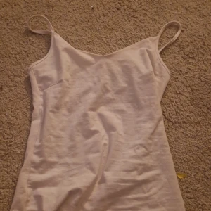 Vit linnetopp med smala axelband - Enkel och stilren vit linnetopp med smala axelband. Perfekt för varma dagar eller som lager under andra plagg. Tidlös design som passar till det mesta och ger en fräsch look.