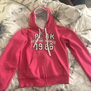 Rosa hoodie Peak Performance S - Säljer en snygg rosa hoodie från Peak Performance i storlek S. Tröjan har vit broderad text och siffror framtill, huva med vita snören och dragkedja hela vägen. Pris kan diskuteras💗