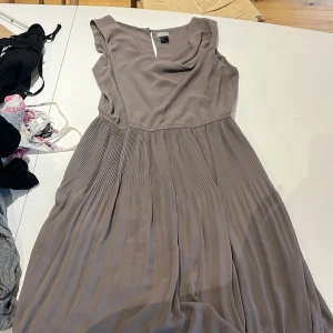 Beige plisserad långklänning H&M - Säljer en snygg beige långklänning från H&M med plisserad kjol och draperad urringning. Klänningen är ärmlös och har en klassisk, elegant look som passar perfekt när du vill känna dig extra fin.