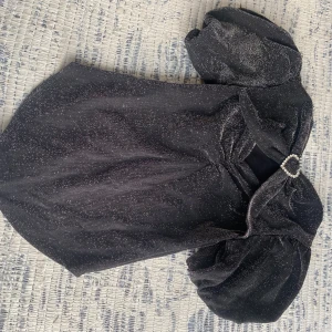 Svart glittrig topp från Zara - Säljer en svart glittrig topp från Zara med puffiga korta ärmar och en pärldetalj därframme✨Den är aldrig använd och nyt pris var 350kr 