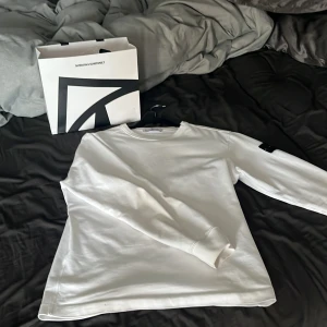 Vit långärmad tröja från Stone Island - Säljer en stilren vit långärmad tröja från Stone Island. Tröjan har en klassisk design med märkets ikoniska logotyp på ärmen. Perfekt för en avslappnad och trendig look.