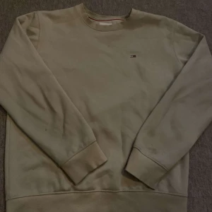 sweatshirt från Tommy Jeans - Säljer en stilren sweatshirt från Tommy Jeans. Tröjan har en liten logotyp på bröstet och ribbade muddar vid ärmslut och nederkant. Perfekt för en avslappnad look.