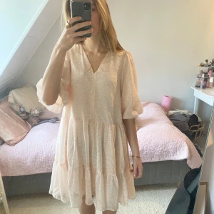 Ljusrosa klänning med volangdetaljer - ESäljer en söt ljusrosa klänning med v-ringning och trekvartsärmar. Klänningen har volangdetaljer och ett subtilt mönster som ger en sommrig känsla. Perfekt för vår och sommar! 🌸 Använd en gång och har en liten fläck (visas på bild)💓