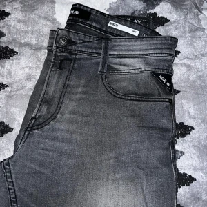 Grå jeans från Replay - Snygga grå jeans från Replay i modellen Anbass. De har en slim fit passform och klassisk femficksdesign. Jeansen har en diskret tvättad look och är perfekta för en stilren vardagsstil. Använd några fåtal gånger men för små.