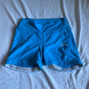 Blå träningsshorts från ICANIWILL - Säljer ett par blå träningsshorts från ICANIWILL. De har en liten scrunch och är tillverkade i ett stretchigt syntetmaterial. Perfekta för gymmet eller löprundan. Snygg och enkel design med ICANIWILL-logga på sidan.