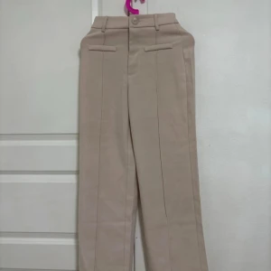 Beige kostymbyxor - Snygga beige kostymbyxor med hög midja och raka ben. Byxorna har diskreta fickor och hällor för bälte. Perfekta för en stilren look.