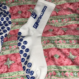 Vita fotbollsstrumpor från FS - Säljer ett par vita fotbollsstrumpor från FS med blå text och logotyp. Strumporna har halkskydd i form av blåa prickar på undersidan, vilket ger extra grepp. Perfekta för fotbollsträning eller match. Också väldigt andnings bara och stretchiga 