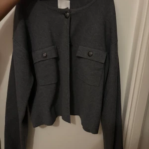 Grå kofta med knappar - Snygg grå kofta med knappar framtill och två fickor med lock. Perfekt för en stilren look. Långärmad och i ett mjukt material.