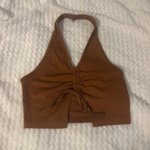 Brun ribbad halterneck-topp - Säljer en snygg brun ribbad halterneck-topp med knytning framtill. Toppen är croppad och har en djup v-ringning. Perfekt för varma sommardagar eller en kväll ute. Passar till både jeans och kjol!