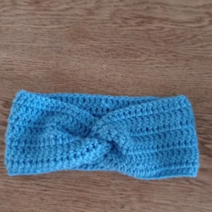 Blå virkad pannband - Snyggt blått virkad pannband med en twistdetalj framtill. Perfekt för att hålla öronen varma under kyliga dagar. Enkel och stilren design som passar till många olika outfits. Hemgjord 