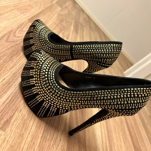 Svarta pumps med guldpaljetter - Snygga svarta pumps dekorerade med glittrande guldpaljetter. Skorna har en hög klack och en rundad tå, vilket ger en elegant look. Perfekta för att ge en glamorös touch till din outfit.