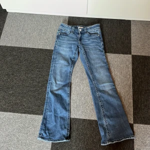 Blå bootcut jeans från Gina Tricot - Säljer ett par snygga blå bootcut jeans från Gina Tricot. De har en klassisk femficksdesign och en knappgylf. Perfekta för en avslappnad stil med en touch av retro.