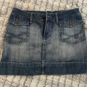 Jeanskjol med fickor - Snygg jeanskjol i klassisk blå denim med två framfickor och två bakfickor. Kjolen har en knapp- och dragkedjestängning framtill och bälteshällor för extra stil. 