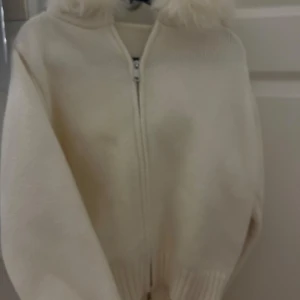 Vit stickad jacka med päls från Alessa - Säljer en mysig vit stickad jacka från Alessa med dragkedja och en huva kantad med päls. Perfekt för vårens kyliga dagar när du vill hålla dig varm och stilren. Jackan har långa ärmar och ribbade muddar för extra komfort. Tror de är one size men passar mig med xs/s och den är helt oanvänd. Köptes för 1800 kr 