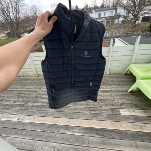 Mörkblå dunväst från U.S. Polo Assn. - Säljer en snygg mörkblå dunväst från U.S. Polo Assn. med dragkedja och två praktiska fickor framtill. Perfekt för kyligare dagar och ger en stilren look. Passar bra till både jeans och t-shirt. Skriv vid minsta fundering😃