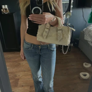 Beige axelväska med kedja - Snygg beige axelväska med kedjedetalj och dubbla handtag. Väskan har en unik textur och stilrena linjer, perfekt för att lyfta din outfit. Den är kompakt men rymmer det viktigaste du behöver ha med dig.