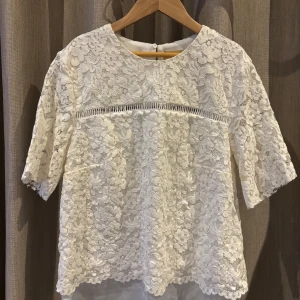 Vit spetsblus med blommönster - Säljer en söt vit spetsblus med blommönster och korta ärmar. Blusen har en fin detalj med spetsband under bysten och en rund halsringning. Perfekt för en somrig look! 🌸