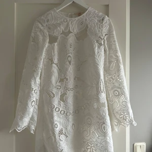 Vit klänning - Säljer en elegant vit klänning från H&M med vackra broderade detaljer. Klänningen har långa ärmar och en rund halsringning. Perfekt för student och avslutnings firande