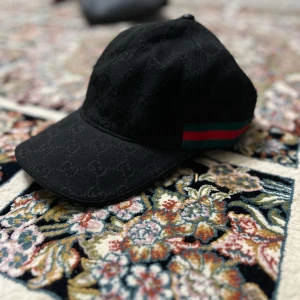 Svart keps med mönster - Snygg svart keps med diskret mönster och ränder i grönt och rött på sidan. Perfekt för en stilren look.