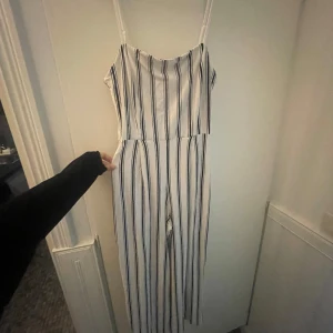 Vit och svart randig jumpsuit från Bershka - Säljer en snygg vit jumpsuit med svarta ränder från Bershka. Den har smala axelband och en bekväm passform. Perfekt för en stilren look! Den passar även som S