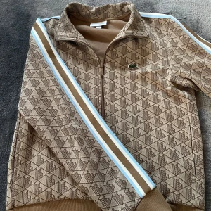 Jacka Lacoste  - Säljer en super snygg jacka från lacoste! Den är köpt i butik på JB:s för 2200 och använts bara några fåtal gånger och är i super skick.  Den har dock ett L på lappen som du ser på sista bilden tyvär.