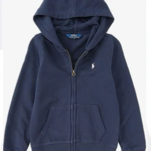 Mörkblå hoodie från Polo Ralph Lauren - Säljer en snygg mörkblå hoodie från Polo Ralph Lauren med dragkedja och klassisk logga på bröstet. Tröjan har en bekväm passform och praktiska fickor framtill. Perfekt för en avslappnad stil.