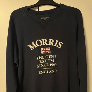 Mörkblå tröja från Morris - Säljer en snygg mörkblå tröja från Morris med tryck framtill. Tröjan har långa ärmar och en rund halsringning. Perfekt för en stilren look.