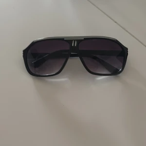 Svarta solglasögon med lila tonade linser - Snygga svarta solglasögon med en klassisk aviatorform och lila tonade linser. Bågarna har en stilren design med silverdetaljer på sidorna. Perfekta för en cool look.