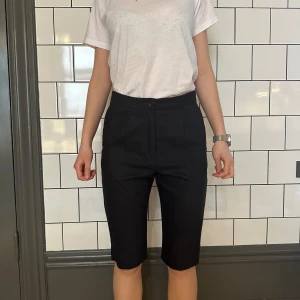 Svarta trekvartsbyxor med pressveck - Snygga svarta trekvartsbyxor från Acne med hög midja och knappdetalj. Perfekta för en stilren look.