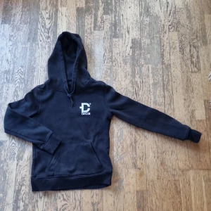 Svart hoodie från DirtCult - Säljer en svart hoodie från DirtCult med tryck både fram och bak. Den har en klassisk känguruficka och justerbar huva med dragsko. Har sprickor I trycket men minns ej om den ska vara så eller tillkommit.  Perfekt för en avslappnad stil. Öppen för prisförslag och fråga gärna.🖤