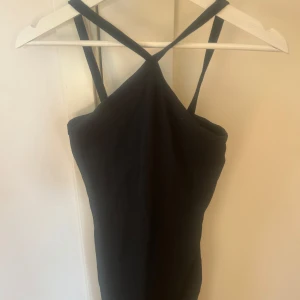 Svart axelbandslös klänning från Lager 157 - Snygg svart klänning med korsade axelband och en elegant passform. Perfekt för en kväll ute eller en speciell tillställning. Klänningen har en stilren design som framhäver figuren.