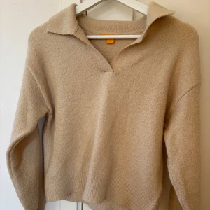 Beige stickad tröja med krage från Gina Tricot - Säljer en mysig beige stickad tröja med en stilren krage och v-ringning. Perfekt för kyligare dagar och ger en avslappnad men ändå elegant look. Tröjan har långa ärmar och ribbade kanter för extra komfort.