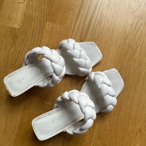 Vita flätade sandaler med klack - Snygga vita sandaler med flätade remmar och fyrkantig tå. De har en låg klack som ger en elegant touch. Perfekta för sommarens alla tillfällen. 8cm hög klack