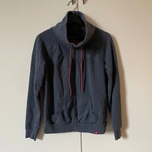 Mörkblå hoodie från EDC - Säljer en mörkblå hoodie från edc med hög krage och dragsko. Tröjan har en stor ficka framtill och är tillverkad i en blandning av bomull och polyester. 
