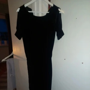 Svart byxdress  - Elegant svart byxdress i mjukt sammetstyg med offshoulder-design. Perfekt för en stilren look.