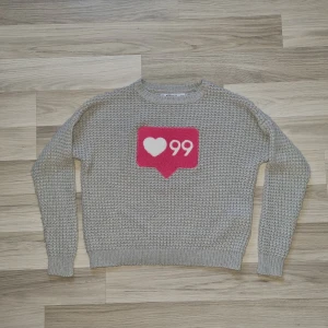 Beige stickad tröja från FB Sister - Säljer en beige stickad tröja från FB Sister med ett coolt rött och vitt motiv på framsidan som liknar en social media notis. Tröjan har långa ärmar och en bekväm passform. Perfekt för en avslappnad stil! 💌