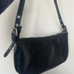 Svart väska med kort band krokodil 🐊  - Väska från HM i en liten och söt stil! Väskan har ett kokodilmotiv som mönster. 