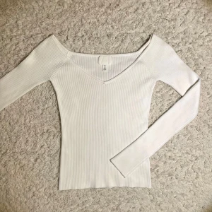 Vit ribbad topp från H&M - Säljer en stilren vit ribbad topp från H&M med v-ringning och långa ärmar. Perfekt för en elegant och enkel look. Passar bra till både jeans och kjol. 🌟