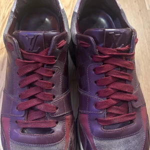 Louis Vuitton skor - Snygga bruna sneakers från Louis Vuitton med röda snören och detaljer. Skorna har en stilren design med LV-logga på plösen och en bekväm sula. Perfekta för en trendig look.