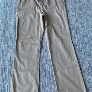 Beige byxor från Calvin Klein - Snygga beige byxor från Calvin Klein i en klassisk stil. Tillverkade av 98% bomull och 2% spandex för en bekväm passform. Perfekta för en stilren look. Beiga chinos i strl 10 (38) från Calvin Klein.  Använd men i fint begagnat skick.  Mått Midjan: ca 44 cm Längd från grenen och ner: ca 81 cm  98% bomull och 2% spandex  Kommer från ett djur och rökfritt hem. 
