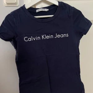 Marinblå t-shirt från Calvin Klein Jeans - Säljer en stilren svart t-shirt från Calvin Klein Jeans med deras ikoniska logga tryckt på framsidan. T-shirten är kortärmad och perfekt för en casual look. Passar utmärkt till jeans eller kjol. 🖤