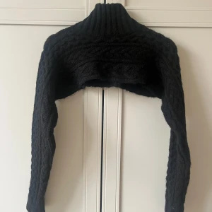 Svart Bolero  - Säljer en svart bolero med grovstickat mönster och hög ribbad krage. Aldrig använd!