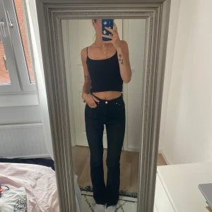 Svarta bootcut jeans med hög midja - Säljer ett par svarta jeans med bootcut-modell och hög midja. Jeansen har klassisk femficksdesign och raka ben som släpper ut lite nertill. Snygg passform och stilren look, perfekta till sneakers eller boots.