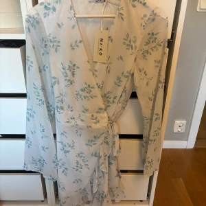 Blommig omlottklänning från NA-KD - Supersöt ljus omlottklänning från NA-KD, helt oanvänd med prislapp kvar!