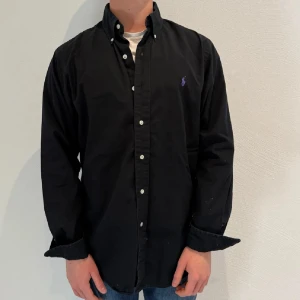 Svart Ralph Lauren Skjorta - Svart Ralph lauren skjorta || Storlek M (Custom Fit) || Skjortan är i bra skick || mitt pris 599kr || Modellen på bilden är 170cm och väger 62kg || tveka inte på att höra av dig vid frågor eller funderingar 