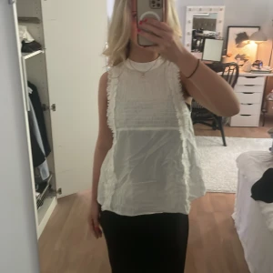 Vit ärmlös blus med spetsdetaljer - Supersöt vit blus i luftig blus med hög hals & den är ärmlös. Modellen på blusen är så snygg och passar till allt!!