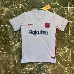 FC Barcelona Nike fotbollströja S - Snygg FC Barcelona fotbollströja från Nike i ljuslila med klubbmärke på bröstet och Rakuten-tryck. Kortärmad modell i lätt och ventilerande material, perfekt för match eller träning. Sidorna har röda och blå detaljer, och Unicef-logga finns på ryggen.