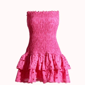 Rosa axelbandslös kortklänning - Supersöt rosa kortklänning med smockad överdel och volangig kjol. Axelbandslös modell som ger en snygg och somrig vibe. Kjolen har broderade detaljer och hålmönster för extra wow-effekt. Perfekt för dig som vill sticka ut! klänningen är helt ny och  har prislapp och ligger i original bagg då jag inte hann skicka tillbaka den. 